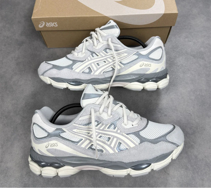 Pair of gray and white running shoes with a brown Asics box on a gray surface